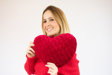 Happy young woman holding a red heart cushion over red background