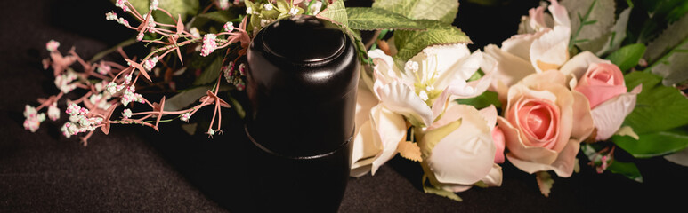 Rose bouquet and urn with ashes on black funeral concept, banner
