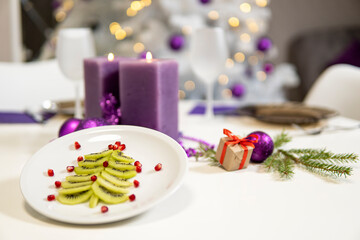 christmas table decoration. kiwi and pomegranate in the shape of a christmas tree on a platter and purple candles