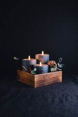 New Year festive decorations with wooden box and black burning candles in a dark interior.