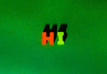 Wooden colorful letters with spelling word text Hi at craft paper green background with shadows and volume, friendly abc greeting