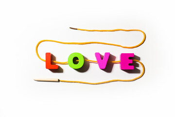 Wooden colorful letters with word Love from colorful letters with holes, strung on a lace in snake shape, with shadows at white background, main word, strong feeling 