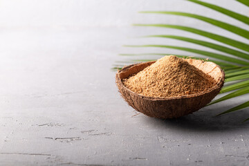 Brown palm or coconut sugar in coconut bowl on grey concrete background