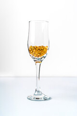 Yellow omega-3 fish oil capsules or vitamin D in a clear glass glass on a white backgroun