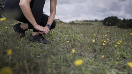 Fototapeta na wymiar Closeup of an athletic Caucasian woman fixing her shoes on a grassy field