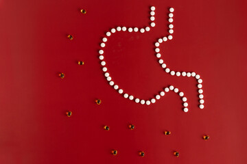 The stomach is laid out of tablets on a maroon background along with yellow drops of vitamins