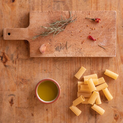 Oil, chili and rosemary on a wooden cutter on a table with some raw rigatoni pasta