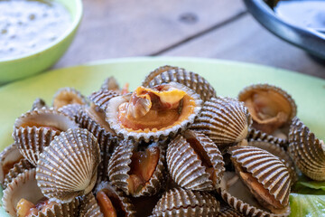 Steamed cockle or Boiled cockles on the dish with spicy seafood sauce and vegetable in restaurante wooden background