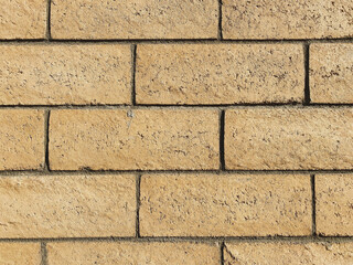 a close out view of tan brick block wall showing grout details, horizontal line design with bright natural sun light enhancing the rough details and textures 

