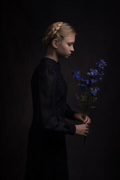 Girl en profile in classic dress with blue flower in hands in dark painterly renaissance style
