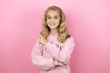 Young beautiful child girl standing over isolated pink background smiling confident pointing with hand and finger to the side