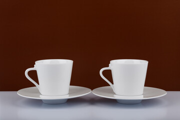 Two coffee cups on white table against brown background
