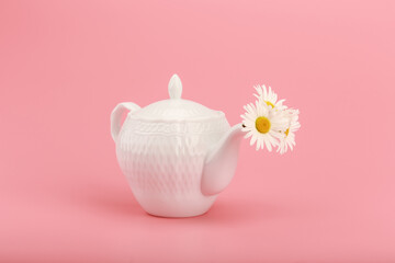 White porcelain teapot with camomile flowers on a pink background. The concept of herbal tea and healthy lifestyle