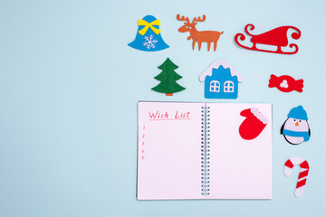 Flat composition with blank open notebook with inscription WISH LIST and christmas toyson blue background