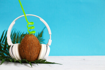 A coconut with straw and headphones on blue background. Summer and trave concept. copy space