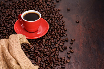 Naklejka premium Red coffee cup with black needle coffee with saucer and fragrant roasted coffee beans on the needle colored table - top view with copy space.
