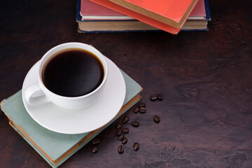 White coffee cup and saucer with dark black coffee pasted on an old book on a needle-colored table - top view with copy space.