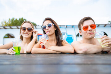 Happy friends enjoying in pool bar. Summer beach party. Drinking tropical alcohol cocktails.