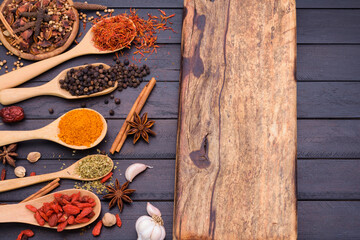 Wooden cutting board and spoons spices chili garlic salt kosher pepper on a dark wooden table. Top view with copy area
