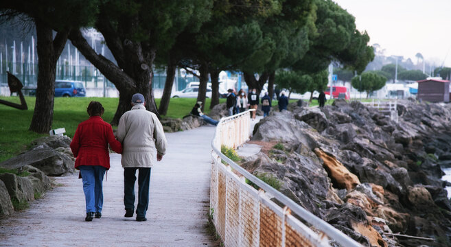 Abuelos paseando por la costa, con unos j&oacute;venes al fondo.