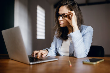 Young beautiful woman in glasses works in the office for a laptop. Handsome office worker. A student studies using a laptop. Doing work on a laptop. Pay for the order via laptop
