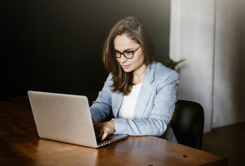 Young beautiful woman in glasses works in the office for a laptop. Handsome office worker. A student studies using a laptop. Doing work on a laptop. Pay for the order via laptop