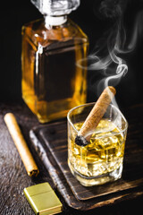 whiskey or bourbon, distilled drink with malt in a glass with ice cubes, with a lighted cigar on the side, soft smoke. Time to relax, lifestyle