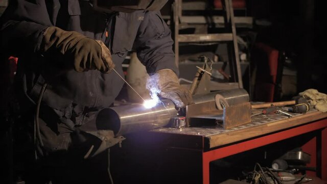 Man shielded metal arc welding stainless steel pipe in workshop. MEDIUM SHOT