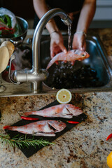 Woman prepares fish for cooking, washes fish, rosemary lemon and fish.
