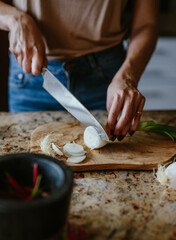 Woman cuts tomatoes onions and hot peppers on a cutting board for cooking.