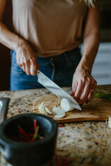 Woman cuts tomatoes onions and hot peppers on a cutting board for cooking.