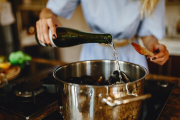 Girl adding white wine to a pan with mussels, woman preparing food