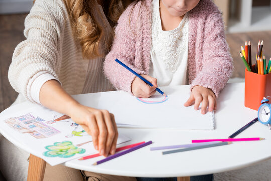 cropped view of little girl drawing pictures with colorful pencils while visiting psychologist, stock image