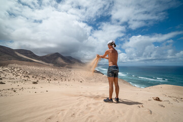 young man takes sand between his hands in Jandia. Fuerteventura