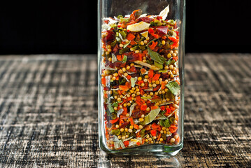 A mixture of various spices in a glass jar close up. Spices and condiments on a black, old shabby board. Free space and copy space for text near condiments.