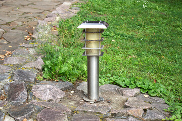 Street steel lamp on a stone paving next to a green lawn