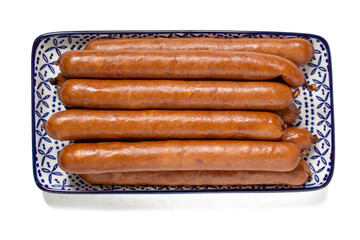 Smoked thin sausages on blue and white plate, close up, isolated on white background