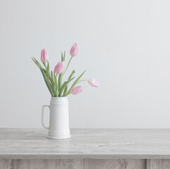 pink tulips in white ceramic jug on wooden table on background white wall