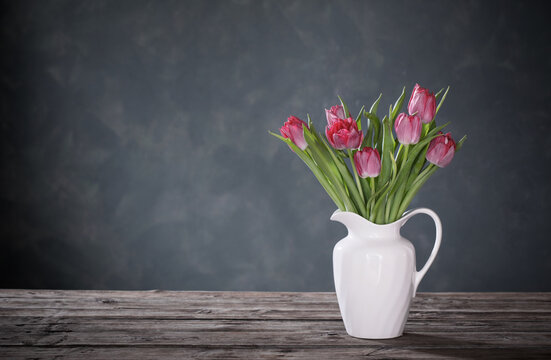 beautiful tulips in white jug on dark background