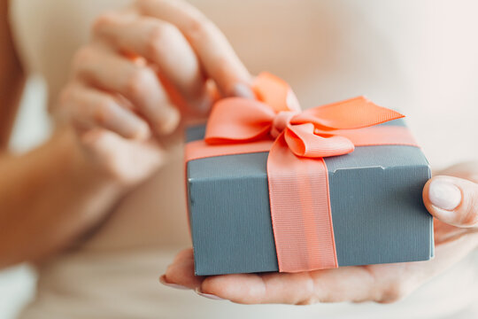 Close-up of female hands holding a small gift wrapped with a satin ribbon