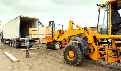 The tractor loads boards, lumber from the finished product warehouse into the container of the truck