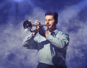 A man in a blue back light and the mist plays the trumpet.