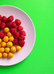 Pink plate with raspberries and yellow berries on green background 