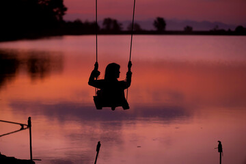 Silhouette of woman Ride on the swing By the lake Twilight