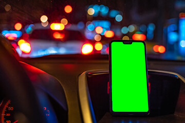 Smart-phone mockup green screen on the car driving at night. GPS during drive. Driving in the city streets at night.
