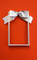 Bright holiday background. An empty silver frame and a bow on a red background. Concept greetings for Christmas, thanksgiving, New year, mother's Day, birthday, Valentine's Day