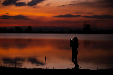 Silhouette of woman  Take a rest, take a photo By the lake at sunset