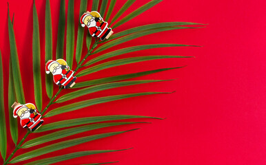 New year's holiday background. Palm branch with wooden figures of Santa Claus on a red background. The view from the top. Greeting card for Christmas.