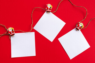 New year's holiday background. White sheets for notes on wooden clothespins with figures of Santa Claus on a red background. The view from the top. Greeting card for Christmas.