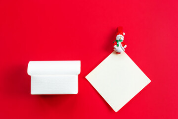 An empty gift box and a white sheet of paper with a snowman figure on a red background. Concept greetings for Christmas, New year. Flat lay, copy space, horizontal cropping